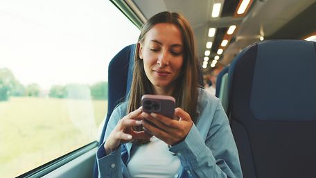 Frau sitzt in einer Regionalbahn und schaut auf ihr Mobiltelefon